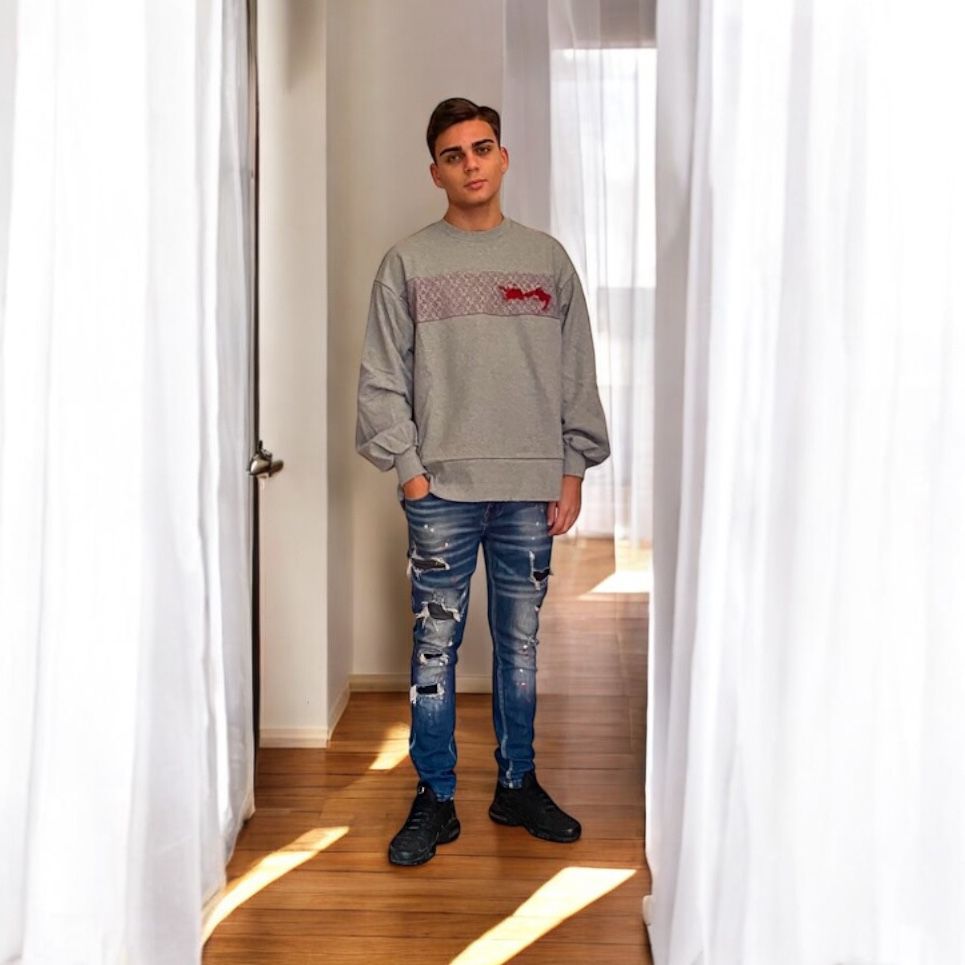 Image of a young man wearing The Lace Embroidered Sweatshirt by Meagratia paired with jeans and black sneakers