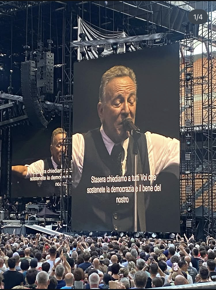 Image of the Bruce Springsteen concert in Milano. The Boss wears a white shirt, dark tie and vest. Subtitles in italian make every word clear.