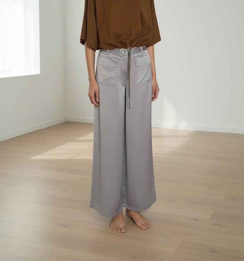 I Pantaloni Fluidi in lavanda abbinati alla Maglia Cropped in caramello. A piedi nudi su un pavimento di legno in uno studio soleggiato con pareti bianche e luce da una finestra laterale.