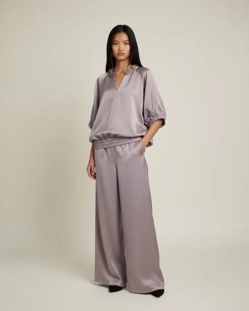 Modella bruna dai capelli lunghi indossa il completo Miaoran in lavanda: la Blusa Fluida abbinato ai Fluid Trousers e scarpe nere a punta. Volume scolpito, intento rilassato, magnetico.