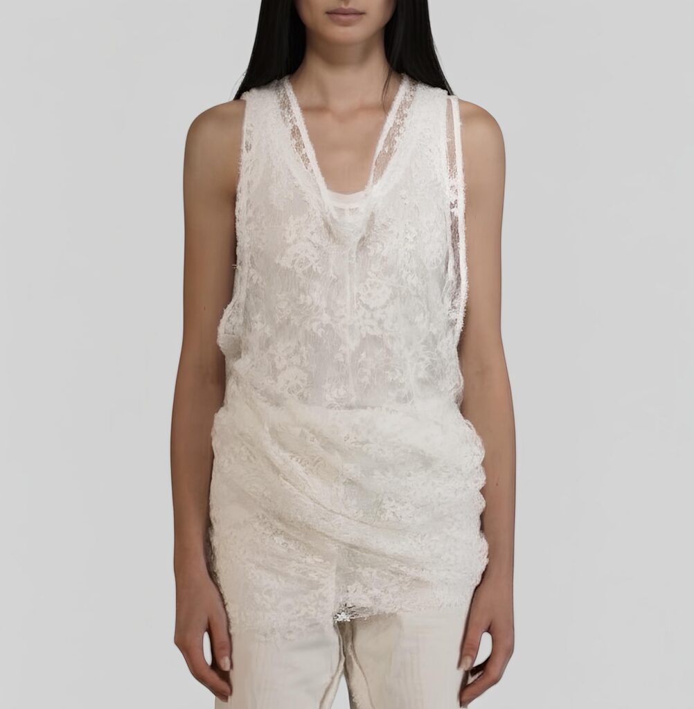 Una modella bruna indossa The Lace Top di Marc Le Bihan. Tank top in pizzo di Venise con scollo rotondo, giromanica ampio e silhouette allungata. Prezioso per il suo ricamo intricato e la texture distintiva. Elegante, versatile, ideale per layering. Senza tempo.