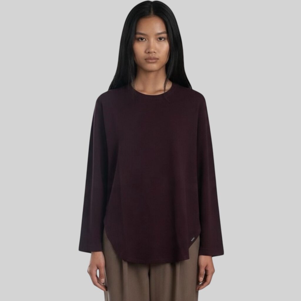 Close-up studio shot of a model wearing the round-hem long-sleeve tee by Ujoh in deep purple, showing the curved hem and sleeve detail.